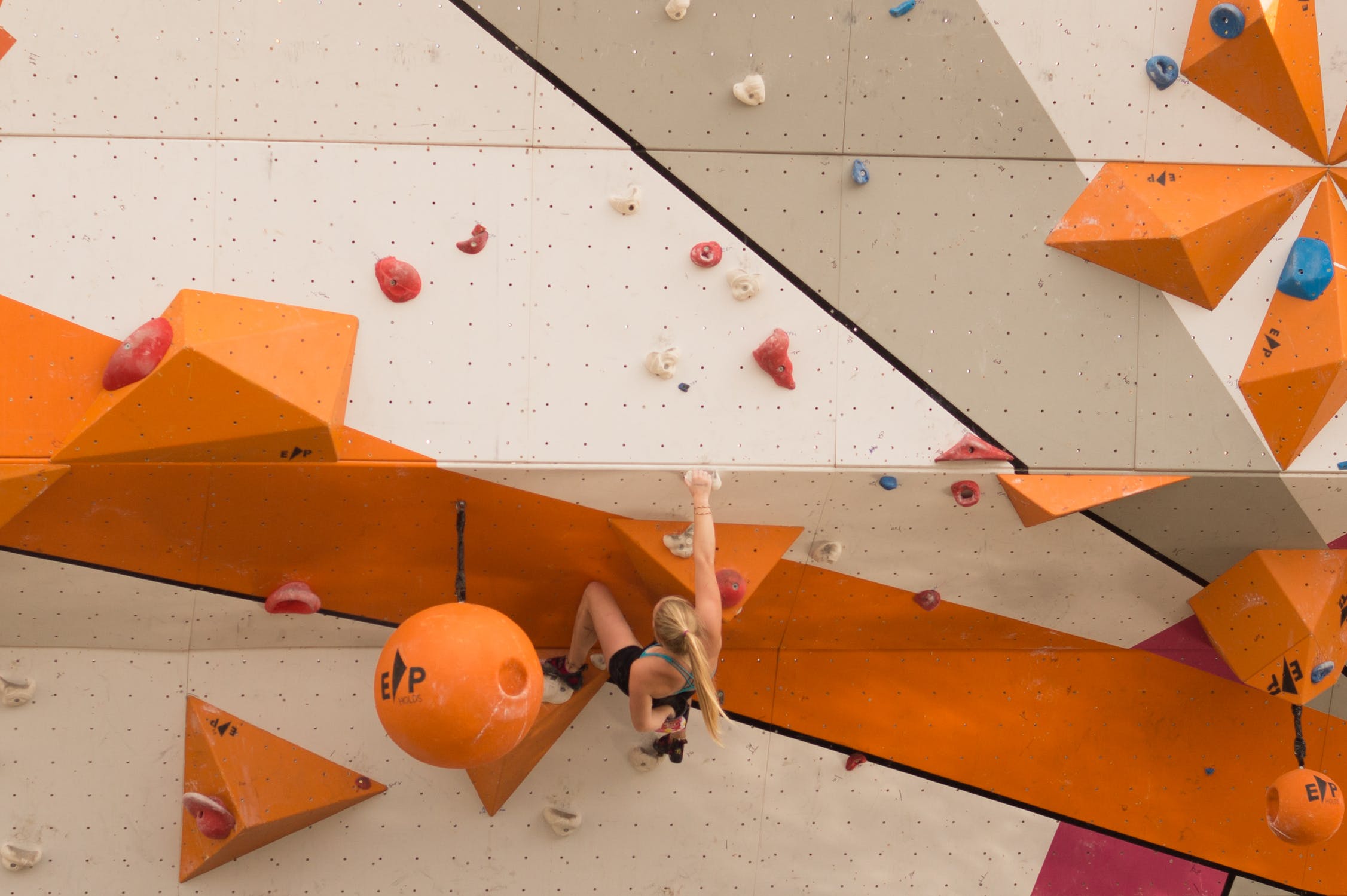 Frau die in einer Kletterhalle eine Wand hoch klettert.