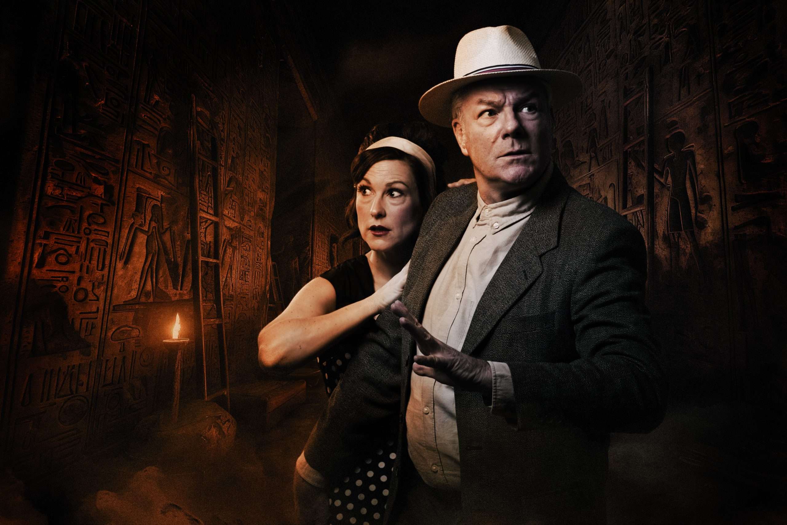 Zwei Abenteurer – ein Mann mit Hut und eine Frau in 50er-Jahre-Kleidung – stehen angespannt in einer altägyptischen Grabkammer voller Hieroglyphen.